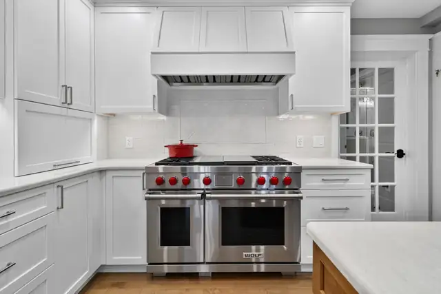 White shaker kitchen with a professional dual-fuel range, white quartz counters and a paneled range hood