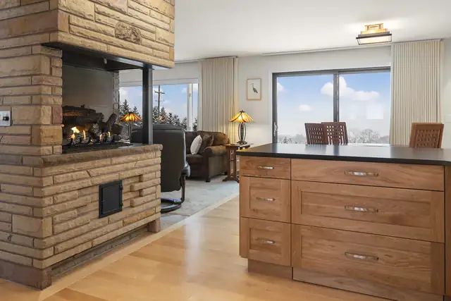 Open kitchen and living room with cherry cabinets, a brick wood stove surround and large windows