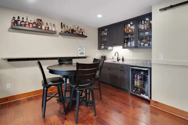 Finished basement in the Finger Lakes region with a dark-cabinet wet bar, bottle shelves and a pub-height table