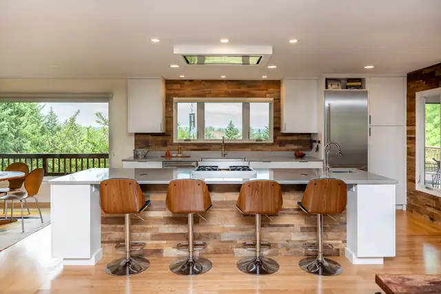 Remodeled kitchen with brown leather stools around a marble-topped island with reclaimed wood paneling and white cabinets