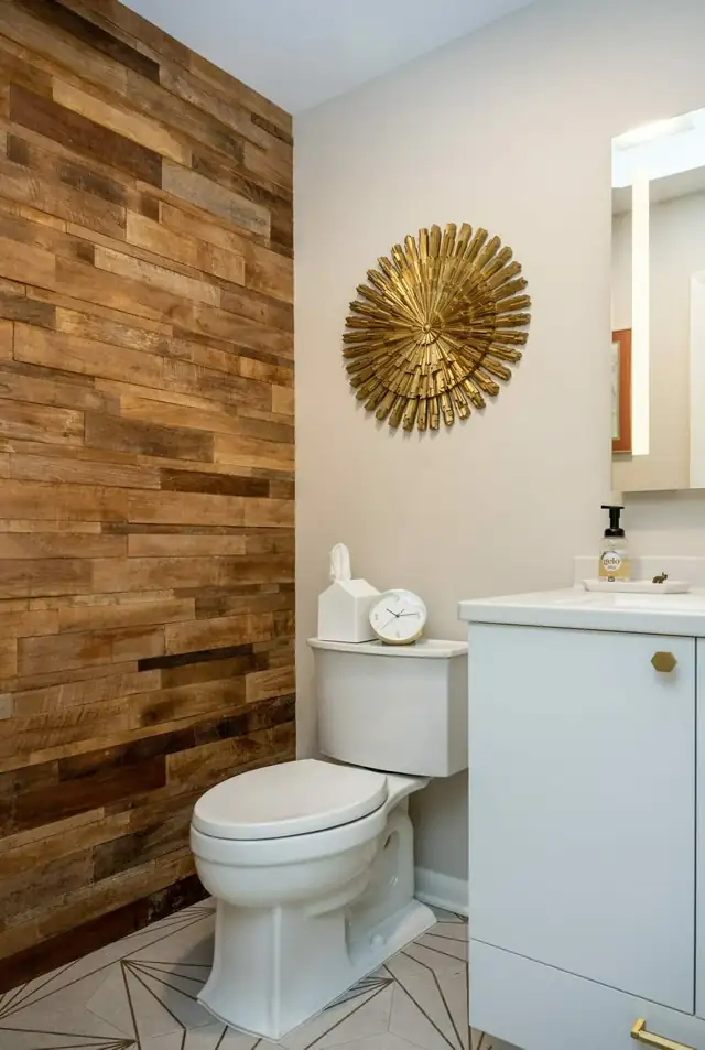 Powder room with a reclaimed wood accent wall, white vanity and gold starburst mirror